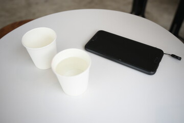 two white paper cups in cafe coffee table with mobile phone