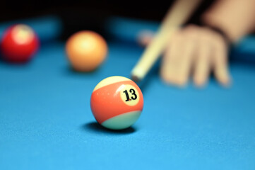 White and orange billiard ball No. 13 on the background of a hand with a cue. Image with selective focus.