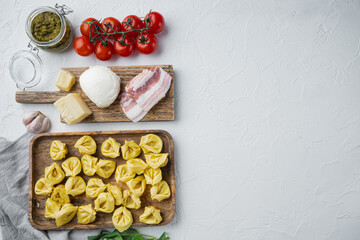 Italian Homemade Tortellini with ingredients, ham, basil, pesto, mozzarella, on wooden tray, on white background, top view flat lay,  with copy space for text