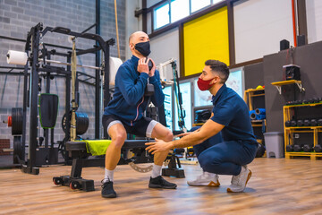 Fototapeta na wymiar Personal trainer in the gym correcting the squats of the young athlete in the coronavirus pandemic, a new normal. With protective face mask