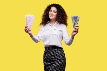 Excited young curly girl holding money with lottery tickets and celebrating success isolated over yellow background