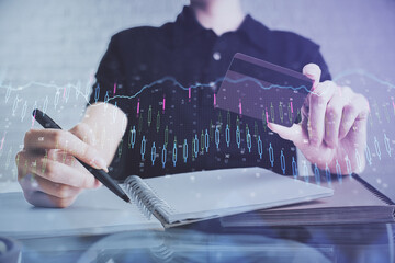 Double exposure of man hands holding a credit card and Forex graph drawing. Stock trading and digital fintech in Internet E-commerce concept.