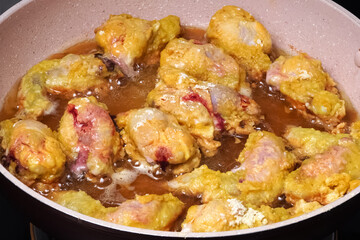 Chicken meat coated with flour is being fried in a frying pan.