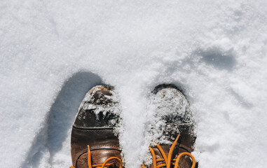 A man in brown leather boots with orange laces stands on white fresh snow in winter. Photography,...