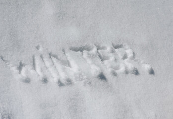 The word winter is written, drawn on white fresh snow. Photo, top view.