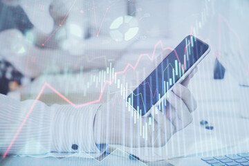Double exposure of man's hands holding and using a digital device and forex graph drawing. Financial market concept.