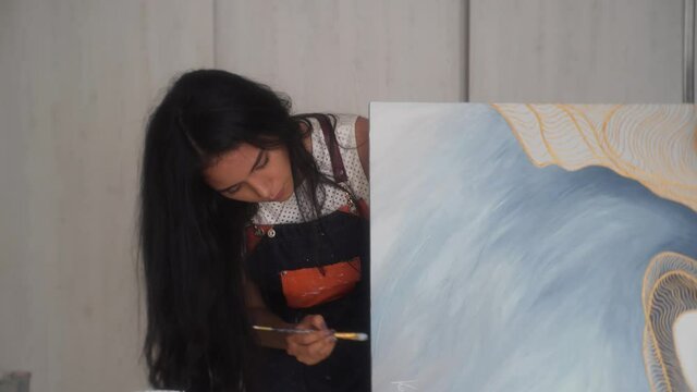 Hispanic Female Painter With Apron Brushing Paint On Side Of Canvas. - close up