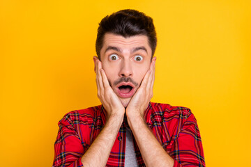 Photo of shocked funky young guy wear checkered shirt arms cheeks open mouth isolated yellow color background
