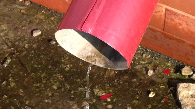 Water flows from a red downspout onto the asphalt, the melting of the snow on the roof