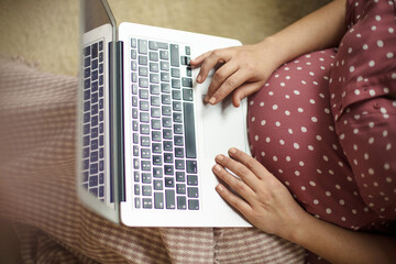 Obraz premium Pregnant woman sitting on floor and using laptop.