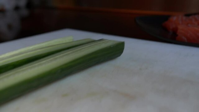Close up view of knife cutting cucumber by length. Vegetable preparation and core removal on a cutting board