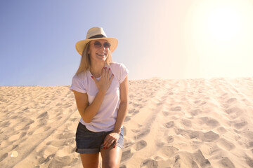 Fototapeta na wymiar Young woman in hat and white t-shirt smiling while standing on the sand in the desert the sun is shining