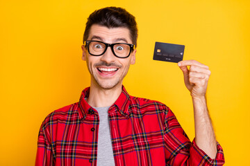 Photo of cheerful positive young guy wear checkered shirt glasses holding bank card isolated yellow color background