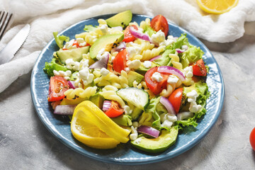 Vegetarian healthy lunch - pasta salad with fresh vegetables, avocado and feta on concrete background