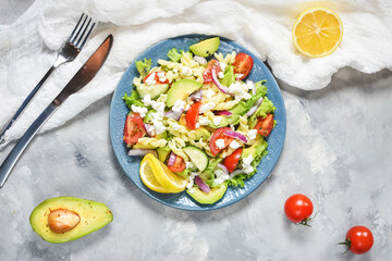 Vegetarian healthy lunch - pasta salad with fresh vegetables, avocado and feta on a concrete background