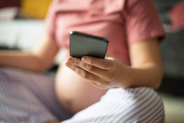 Pregnant woman sitting on floor at home and using mobile phone.