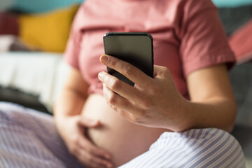 Pregnant woman sitting on floor at home and using mobile phone.