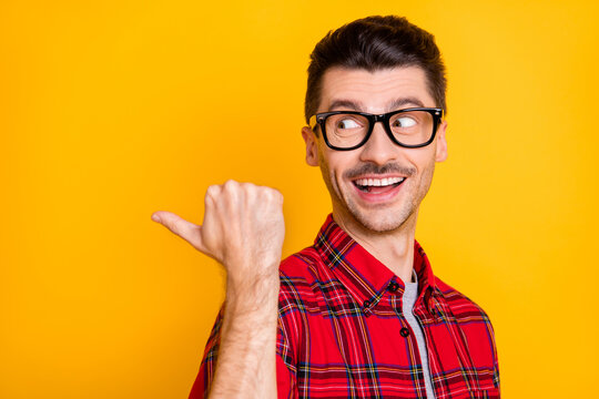Photo of impressed cute young man dressed plaid shirt spectacles pointing thumb up back empty space isolated yellow color background