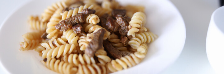 Pasta and meat are on plate. Two white plate of food stand on white table. Cooking delicacies at home. Food order online concept.