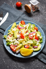 Vegetarian healthy lunch - pasta salad with fresh vegetables, avocado and feta on black stone background