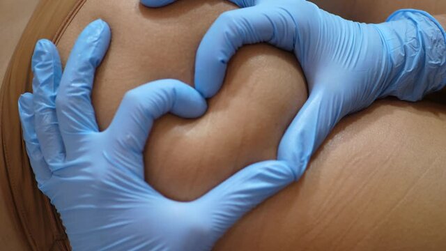 Female hands in gloves make a heart shape on the buttocks, refocusing the shot. Massage with love