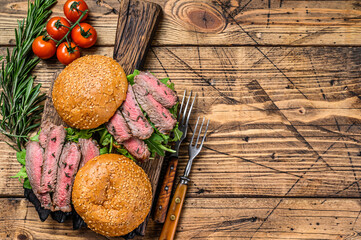 Burger sandwich with beef steak cuts, arugula and spinach. wooden background. Top view. Copy space