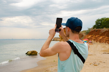 Man catching signal on the wild beach, making photo of seascape. back wiew