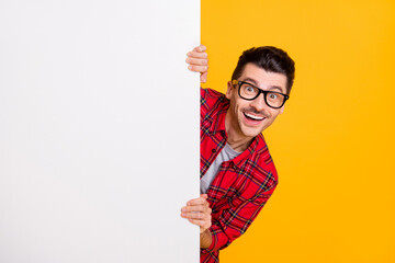 Photo of young happy positive good mood man in glasses hold big white banner isolated on yellow...