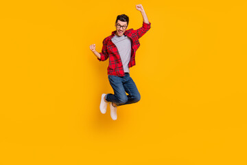 Fototapeta na wymiar Full length photo of lucky young guy dressed plaid shirt eyeglasses jumping high rising fists isolated yellow color background