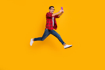 Fototapeta na wymiar Full length photo of cute young guy dressed plaid shirt eyeglasses jumping holding modern device isolated yellow color background