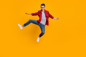 Fototapeta na wymiar Full length photo of funny young guy dressed plaid shirt eyeglasses jumping high isolated yellow color background