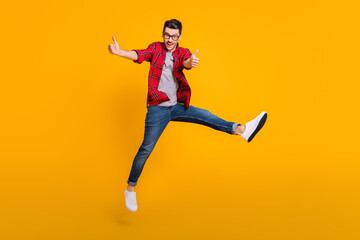 Fototapeta na wymiar Full body photo of brunette man make thumbs up jump air wear jeans glasses isolated on yellow color background