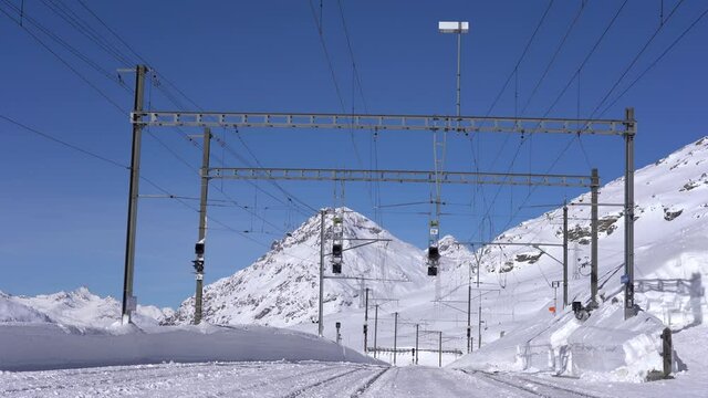 Switzerland Alps , Poschiavo - February 2021 Bernina Express, red train of Bernina pass in Ospizio Bernina station -  Unesco world heritage - Rhaetian railway with snow in a sunny day with blue sky