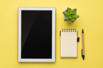 Photo overhead of tablet notebook pen and plant isolated on the yellow background