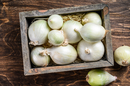 Raw fresh white onion in wooden box. Wooden background. Top view
