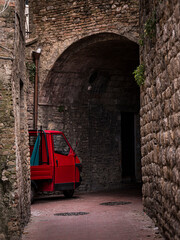 Red colored motorcycle parked in a narrow street of a medieval town in Italy