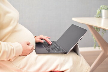 Naklejka premium A pregnant woman in her twenties works from home using a laptop with fear of coronavirus and flu virus.