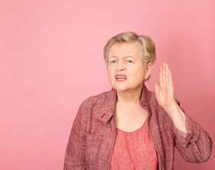 Elderly woman with hearing problem on pink background. Portrait of grandmother trying to hear something.