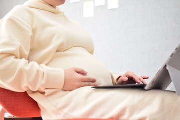 Naklejka premium A pregnant woman in her twenties works from home using a laptop with fear of coronavirus and flu virus.