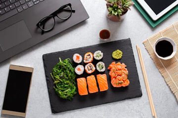 Sushi takeaway at work desk with laptop overhead. Eating sushi for lunch break at office, lunch meal at work, top view