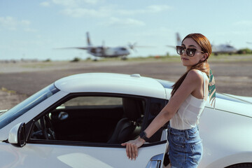 Naklejka premium Beautiful girl in sunglasses on the background car and airplane 