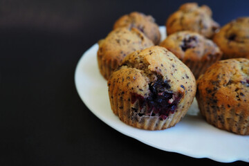 seven muffins with cherries, small pieces of dark chocolate, rice flour, cornmeal, eggs and yogurt lie on a white plate on a black background side view . homemade gluten-free cupcakes