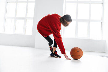 Naklejka premium Athletic young sportswoman working out with basketball indoors