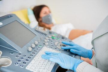 Gynecologist doctor wearing protection face mask does ultrasound, sonogram procedure to a pregnant woman. Pandemic time and health care concept.