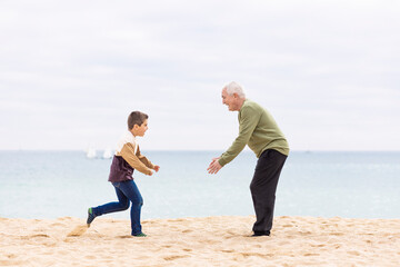 Happy boy running to hug his grandfather on the beach