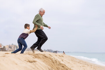 Funny boy pushing his grandfather on the beach