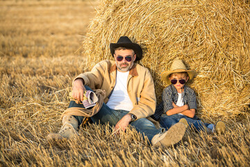 Naklejka na ściany i meble Father and son resting in the field wear hats, shirts and jeans. Son like as father concept