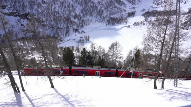 Switzerland Alps , Poschiavo - February 2021 Bernina Express, red train of Bernina pass in Alp Grum station -  Unesco world heritage - Rhaetian railway with snow in a sunny day with blue sky