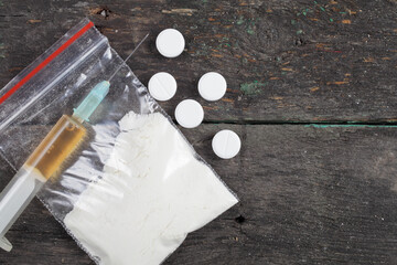 syringe with heroin and pills on a wooden background, place for text