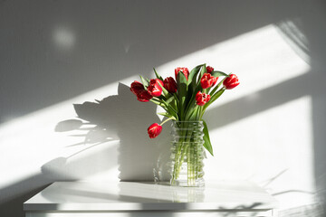 A bouquet of red tulips on a chest of drawers in the room..